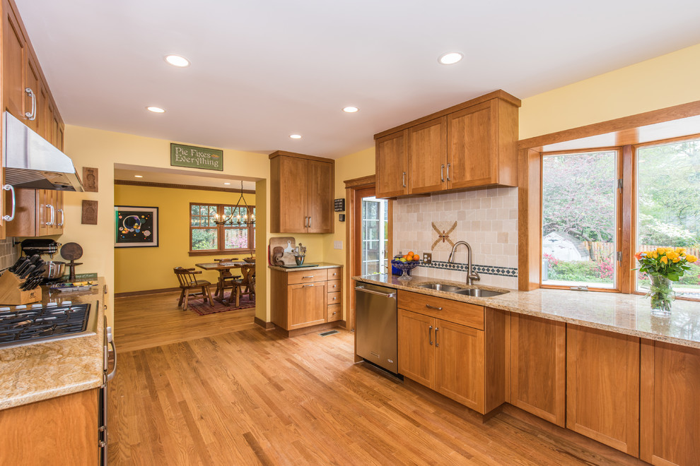 Photo of a large arts and crafts u-shaped separate kitchen in DC Metro with an undermount sink, recessed-panel cabinets, brown cabinets, granite benchtops, beige splashback, terra-cotta splashback, stainless steel appliances, light hardwood floors and brown floor.
