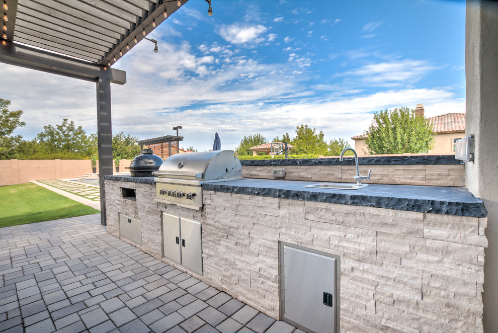 This is an example of a large contemporary backyard patio in Phoenix with an outdoor kitchen, concrete pavers and a roof extension.