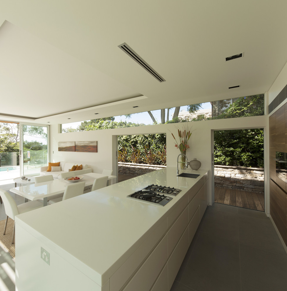 Mid-sized modern galley open plan kitchen in Sydney with an undermount sink, flat-panel cabinets, black appliances, with island and grey floor.