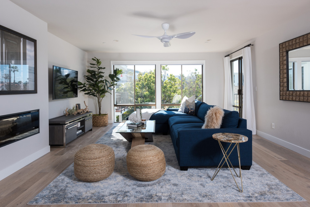 Inspiration for a mid-sized beach style open concept family room in San Diego with a wall-mounted tv, brown floor, grey walls, medium hardwood floors and a ribbon fireplace.