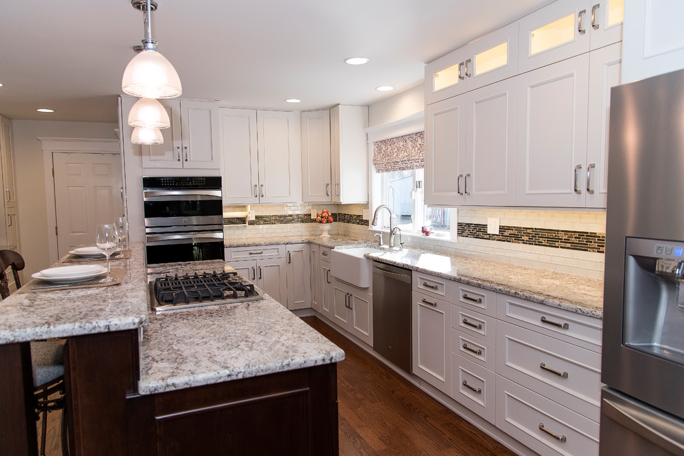 Eat-in kitchen - large transitional l-shaped medium tone wood floor and brown floor eat-in kitchen idea in Baltimore with a farmhouse sink, shaker cabinets, white cabinets, granite countertops, white backsplash, glass tile backsplash, stainless steel appliances and an island