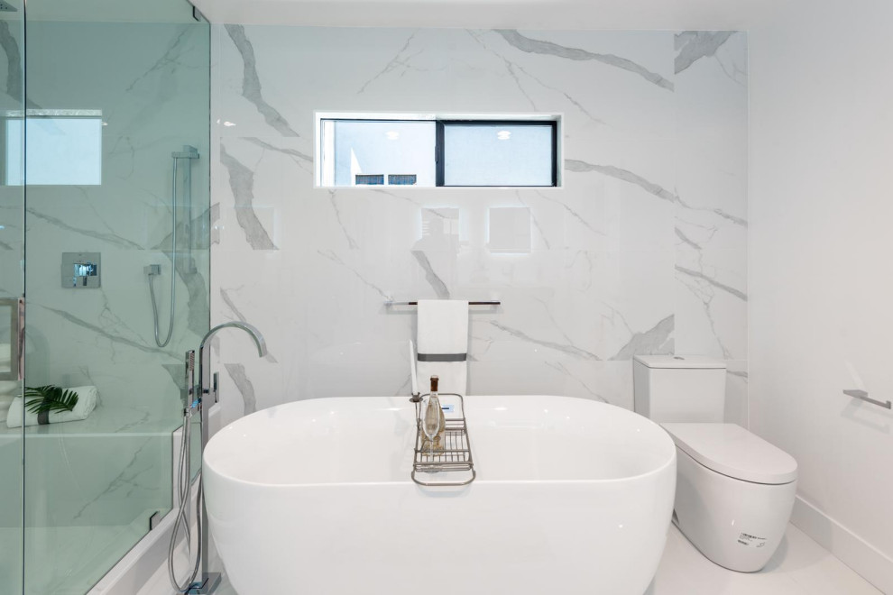 Photo of a large transitional master bathroom in Orange County with a drop-in tub, an alcove shower, a one-piece toilet, white tile, marble, white walls, porcelain floors, white floor, a hinged shower door and exposed beam.
