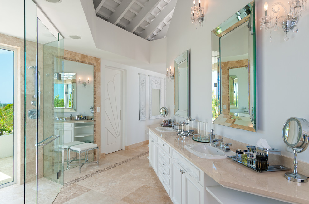 This is an example of a tropical master bathroom in Miami with a drop-in sink, recessed-panel cabinets, white cabinets, a curbless shower, beige tile and white walls.