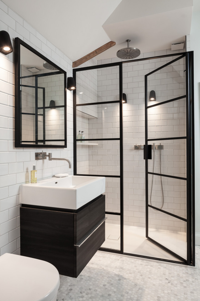 Photo of a mid-sized transitional 3/4 bathroom in London with flat-panel cabinets, dark wood cabinets, an alcove shower, a wall-mount toilet, white tile, subway tile, white walls, ceramic floors, an integrated sink, solid surface benchtops, grey floor, a hinged shower door and white benchtops.