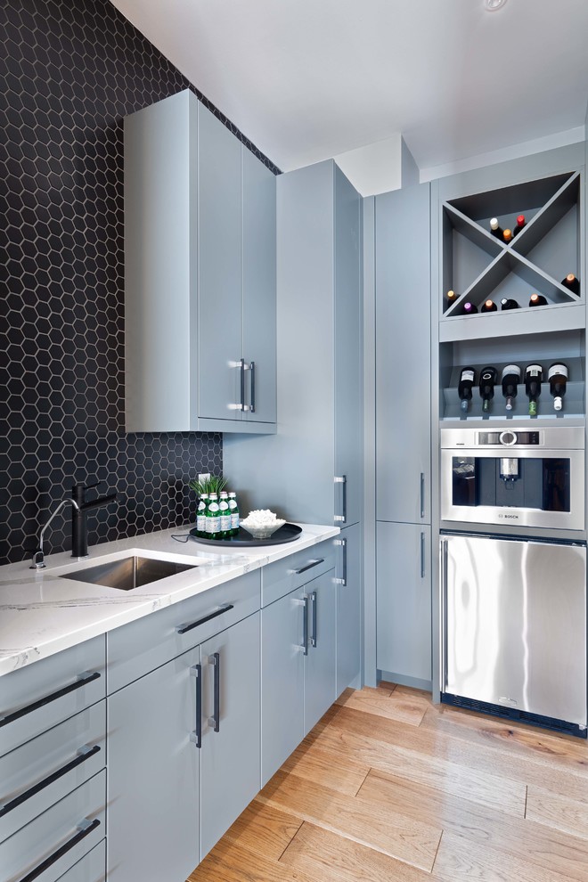 This is an example of a mid-sized contemporary wet bar in Ottawa with an undermount sink, flat-panel cabinets, grey cabinets, quartz benchtops, black splashback, ceramic splashback, medium hardwood floors and white benchtop.