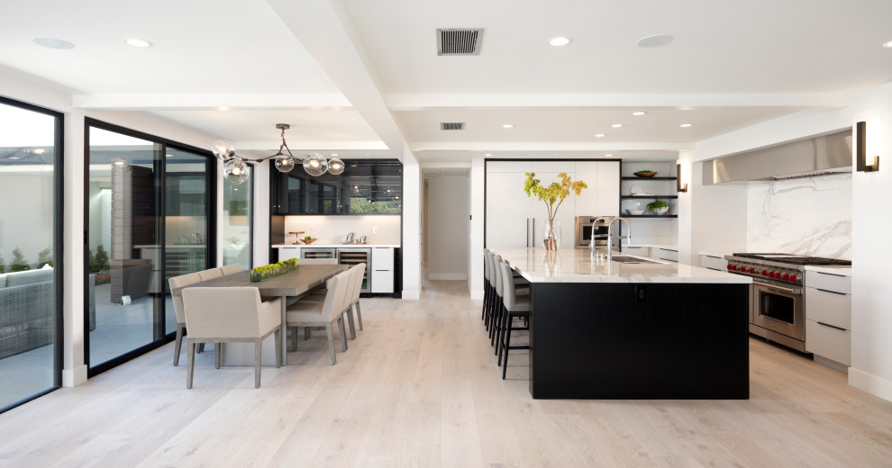 Large contemporary u-shaped eat-in kitchen in Orange County with an undermount sink, flat-panel cabinets, black cabinets, marble benchtops, white splashback, stone slab splashback, stainless steel appliances, light hardwood floors, with island, grey floor and white benchtop.