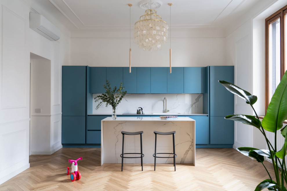 Mid-sized contemporary single-wall open plan kitchen in Milan with a single-bowl sink, flat-panel cabinets, blue cabinets, marble benchtops, white splashback, ceramic splashback, light hardwood floors, with island, brown floor and white benchtop.