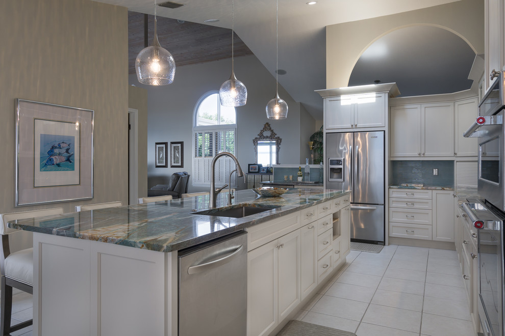 Inspiration for a mid-sized beach style l-shaped eat-in kitchen in Tampa with an undermount sink, recessed-panel cabinets, white cabinets, onyx benchtops, blue splashback, glass tile splashback, stainless steel appliances and with island.