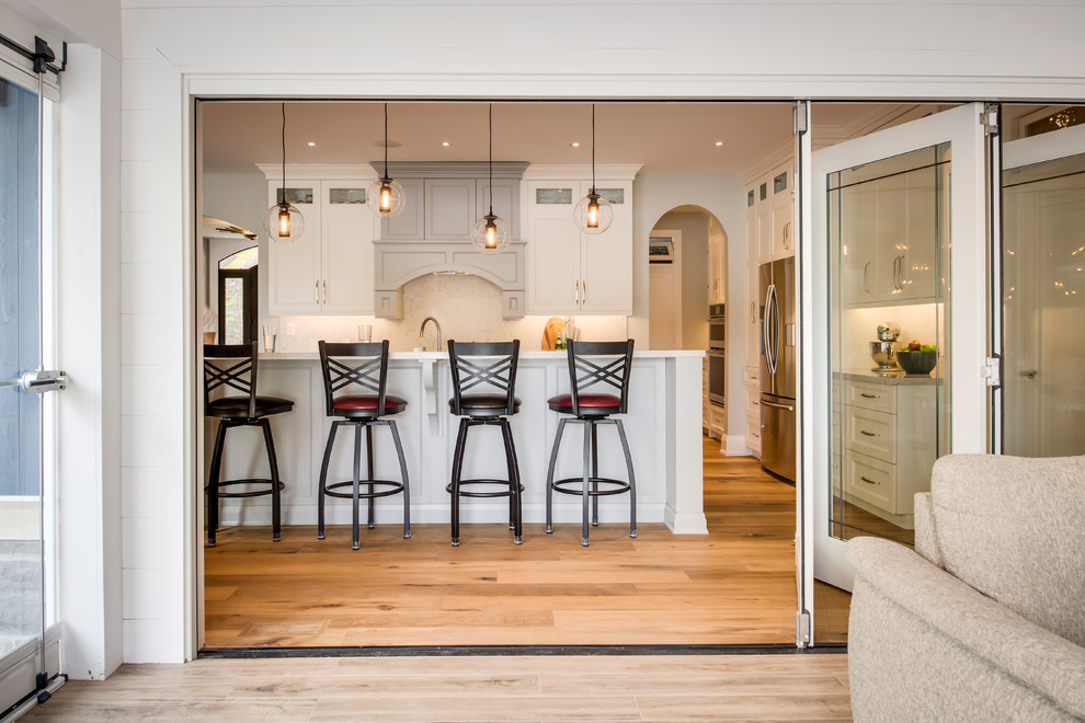 Mid-sized transitional u-shaped light wood floor and brown floor eat-in kitchen photo with an undermount sink, shaker cabinets, granite countertops, multicolored backsplash, stainless steel appliances, an island and white cabinets