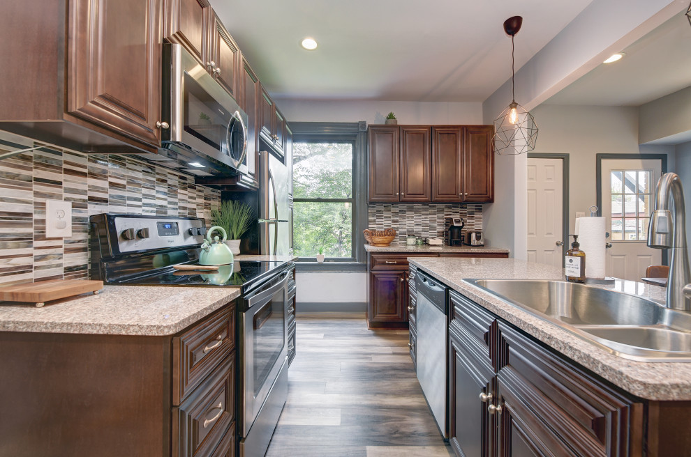 Example of a mid-sized transitional l-shaped gray floor open concept kitchen design with a double-bowl sink, raised-panel cabinets, dark wood cabinets, granite countertops, gray backsplash, matchstick tile backsplash, stainless steel appliances, an island and beige countertops