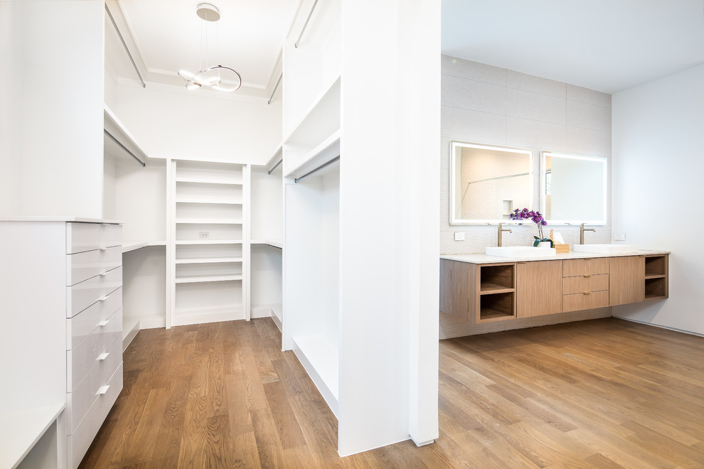 This is an example of a mid-sized modern gender-neutral walk-in wardrobe in Dallas with open cabinets, white cabinets, medium hardwood floors and brown floor.