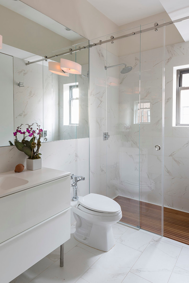 This is an example of a contemporary bathroom in New York with an integrated sink, flat-panel cabinets, white cabinets, a curbless shower, a one-piece toilet and white walls.