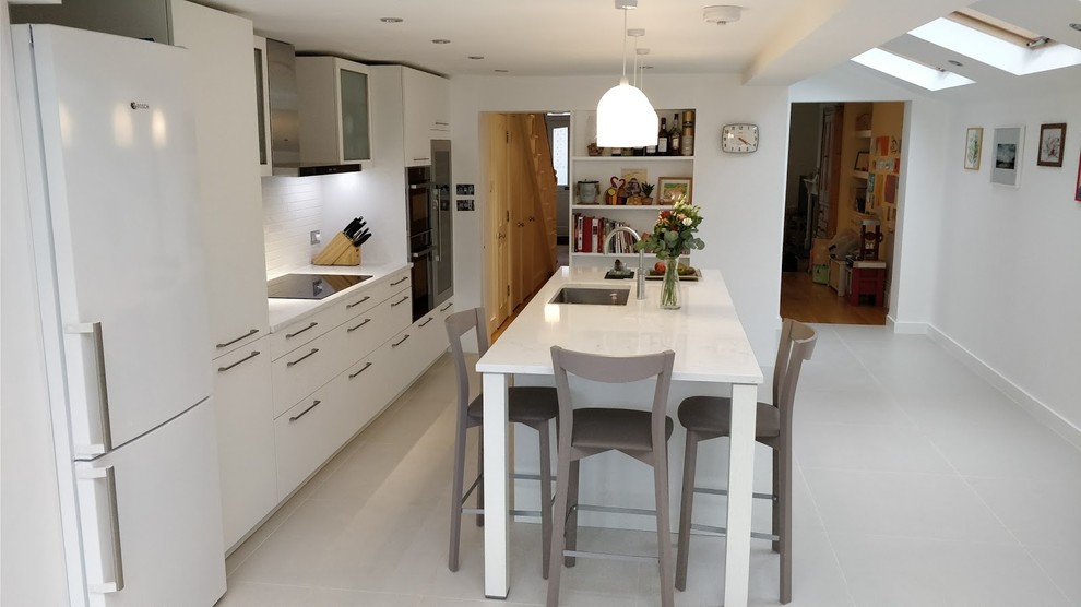 Photo of a mid-sized contemporary single-wall open plan kitchen in London with an undermount sink, shaker cabinets, white cabinets, quartzite benchtops, white splashback, black appliances and a peninsula.