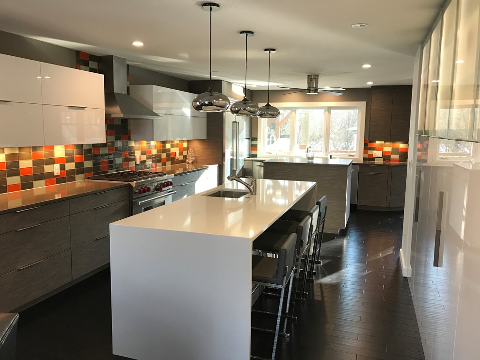 This is an example of a large modern kitchen in Milwaukee with a farmhouse sink, grey cabinets, quartz benchtops, grey splashback, glass tile splashback, stainless steel appliances, dark hardwood floors, multiple islands and brown floor.