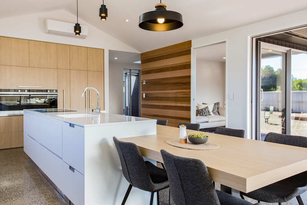 This is an example of a large modern single-wall eat-in kitchen in Christchurch with flat-panel cabinets, quartz benchtops, concrete floors, with island, a single-bowl sink, white cabinets, window splashback, stainless steel appliances, multi-coloured floor and white benchtop.