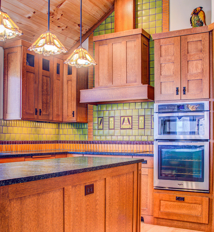 Inspiration for a large arts and crafts l-shaped kitchen in Detroit with an undermount sink, recessed-panel cabinets, medium wood cabinets, granite benchtops, green splashback, ceramic splashback, stainless steel appliances, light hardwood floors and with island.