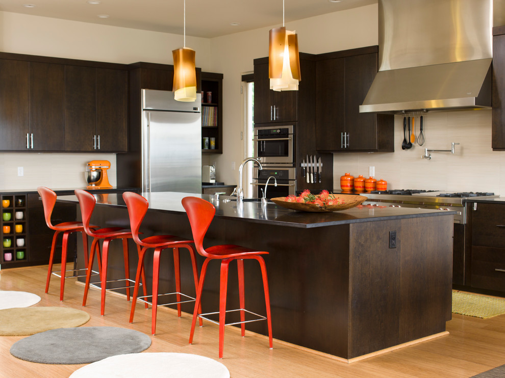 Inspiration for a midcentury l-shaped kitchen in Seattle with dark wood cabinets, granite benchtops, stainless steel appliances, light hardwood floors, with island, flat-panel cabinets, beige splashback and stone slab splashback.