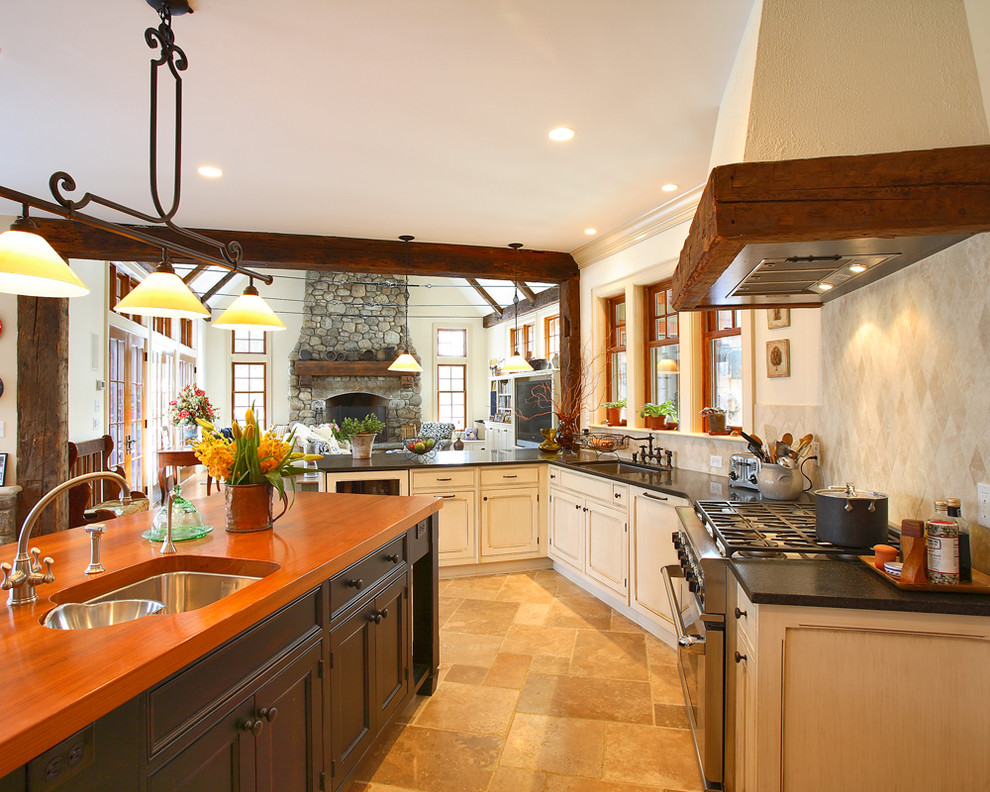 Country kitchen in New York with recessed-panel cabinets, dark wood cabinets, wood benchtops, beige splashback, stone tile splashback, stainless steel appliances, limestone floors and with island.