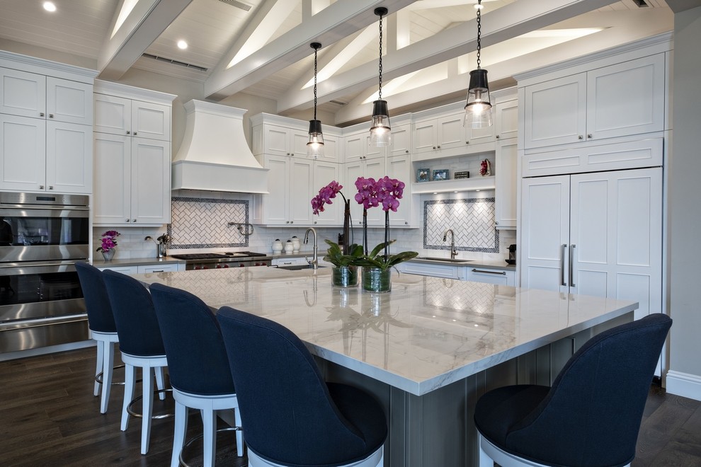 Design ideas for a beach style l-shaped kitchen in Miami with an undermount sink, recessed-panel cabinets, white cabinets, white splashback, panelled appliances, dark hardwood floors, with island and white benchtop.