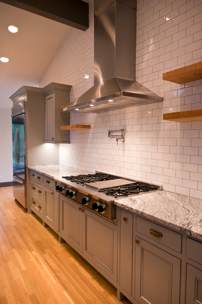 Large industrial single-wall open plan kitchen in Seattle with a farmhouse sink, beaded inset cabinets, grey cabinets, granite benchtops, white splashback, porcelain splashback, stainless steel appliances, light hardwood floors and multiple islands.