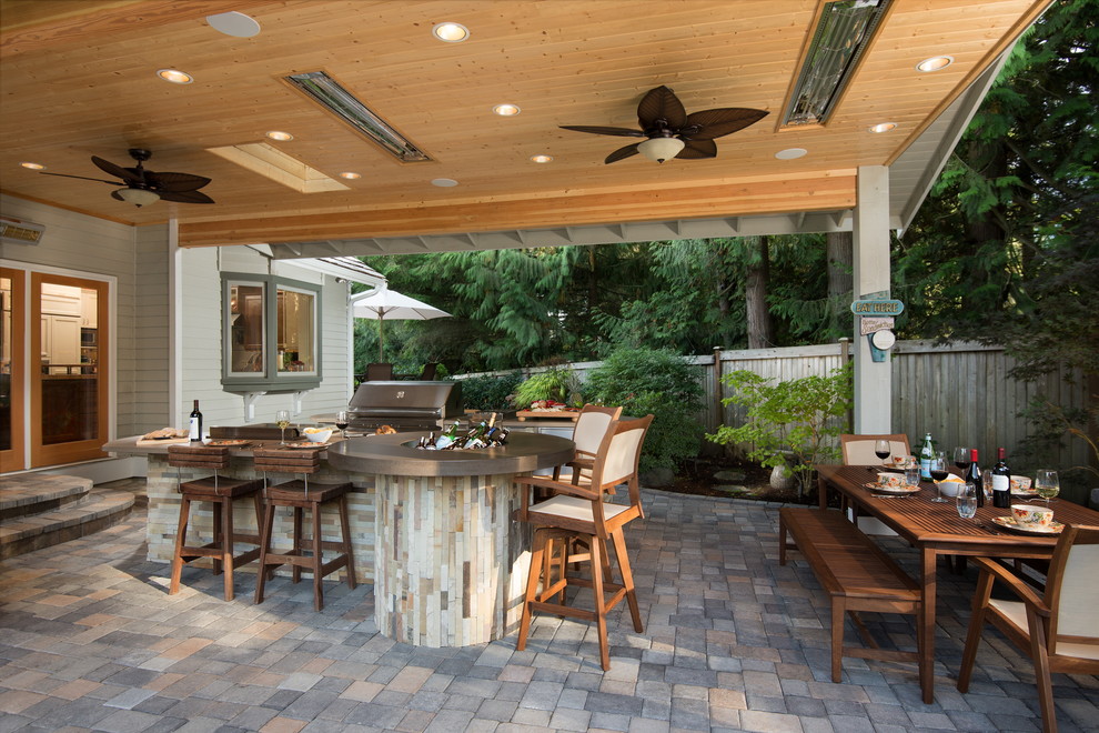 Large country backyard patio in Seattle with an outdoor kitchen, brick pavers and a roof extension.