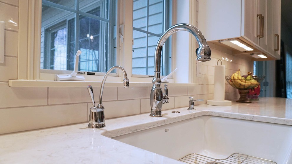 Example of a transitional light wood floor open concept kitchen design with a farmhouse sink, recessed-panel cabinets, white cabinets, white backsplash, subway tile backsplash, stainless steel appliances, an island and white countertops