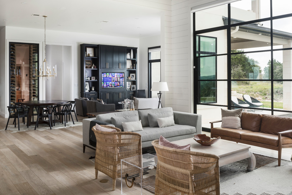 Large transitional open concept living room in Austin with light hardwood floors, a built-in media wall, white walls and beige floor.