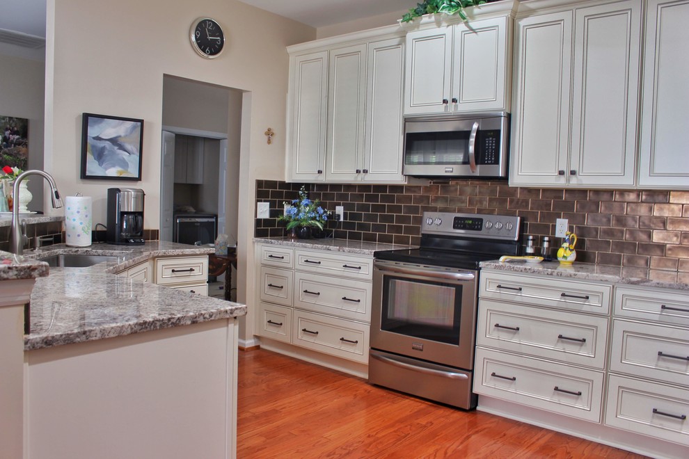 Mid-sized u-shaped medium tone wood floor and brown floor kitchen photo in Charleston with an undermount sink, raised-panel cabinets, beige cabinets, granite countertops, brown backsplash, ceramic backsplash, stainless steel appliances and beige countertops