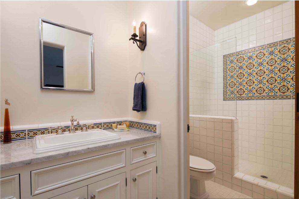 Design ideas for a large mediterranean master bathroom in Santa Barbara with beaded inset cabinets, white cabinets, an open shower, a two-piece toilet, white tile, multi-coloured tile, porcelain tile, white walls, porcelain floors, a drop-in sink and marble benchtops.