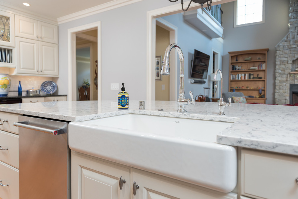 Open concept kitchen - large transitional single-wall light wood floor and brown floor open concept kitchen idea with a farmhouse sink, raised-panel cabinets, white cabinets, quartz countertops, white backsplash, ceramic backsplash, stainless steel appliances, an island and white countertops