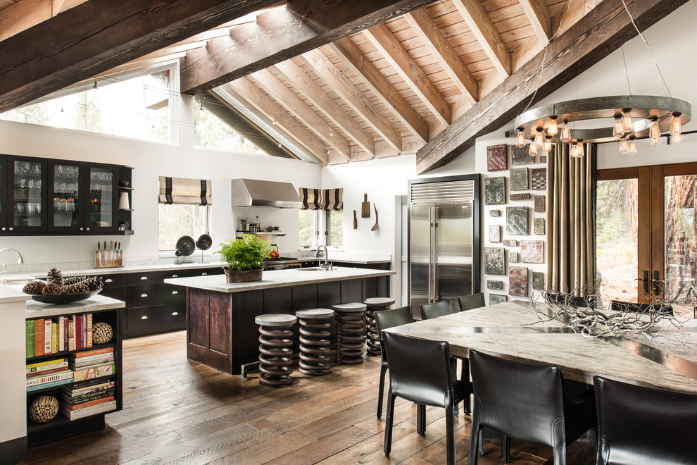 This is an example of a large industrial l-shaped eat-in kitchen in Sacramento with glass-front cabinets, black cabinets, stainless steel appliances, medium hardwood floors, with island, an undermount sink, quartz benchtops and white splashback.