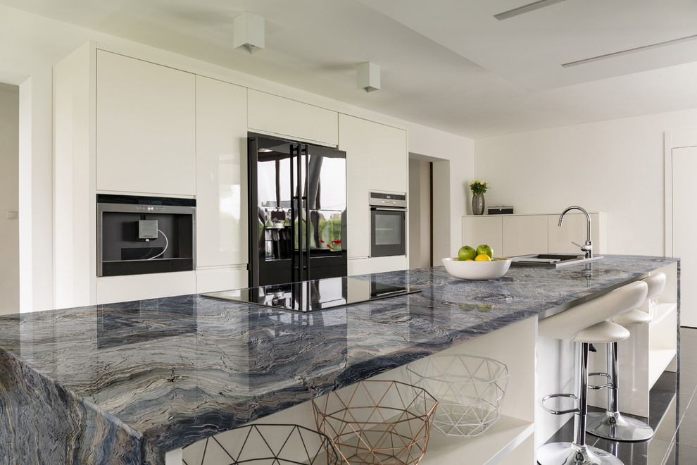 This is an example of a modern open plan kitchen in Miami with an undermount sink, white cabinets, quartzite benchtops, black appliances, porcelain floors, with island, black floor and blue benchtop.