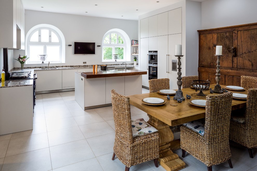 This is an example of a mid-sized contemporary u-shaped eat-in kitchen in Devon with flat-panel cabinets, white cabinets, granite benchtops, porcelain floors, with island, panelled appliances and beige floor.