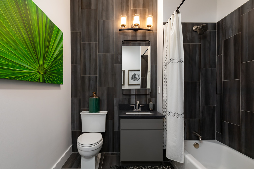 Contemporary bathroom in New York with flat-panel cabinets, grey cabinets, an alcove tub, a shower/bathtub combo, a two-piece toilet, black tile, black walls, an undermount sink, black floor, a shower curtain and black benchtops.