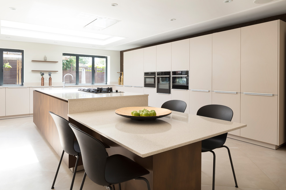 Large contemporary l-shaped eat-in kitchen in London with an integrated sink, flat-panel cabinets, beige cabinets, quartzite benchtops, beige splashback, stone slab splashback, black appliances, porcelain floors, with island, beige floor and beige benchtop.