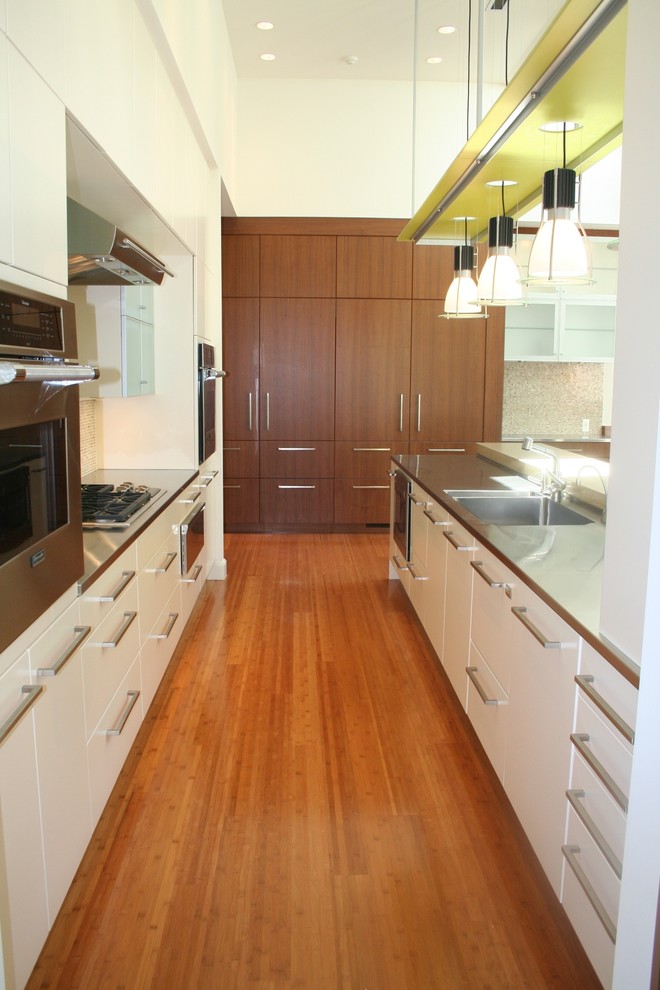 Mid-sized modern galley kitchen in Detroit with an integrated sink, flat-panel cabinets, stainless steel benchtops, panelled appliances, light hardwood floors and a peninsula.
