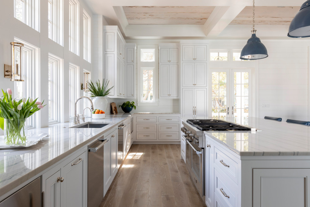 Large beach style u-shaped open plan kitchen in Other with a farmhouse sink, recessed-panel cabinets, white cabinets, marble benchtops, white splashback, subway tile splashback, stainless steel appliances, light hardwood floors, with island, beige floor, white benchtop and coffered.