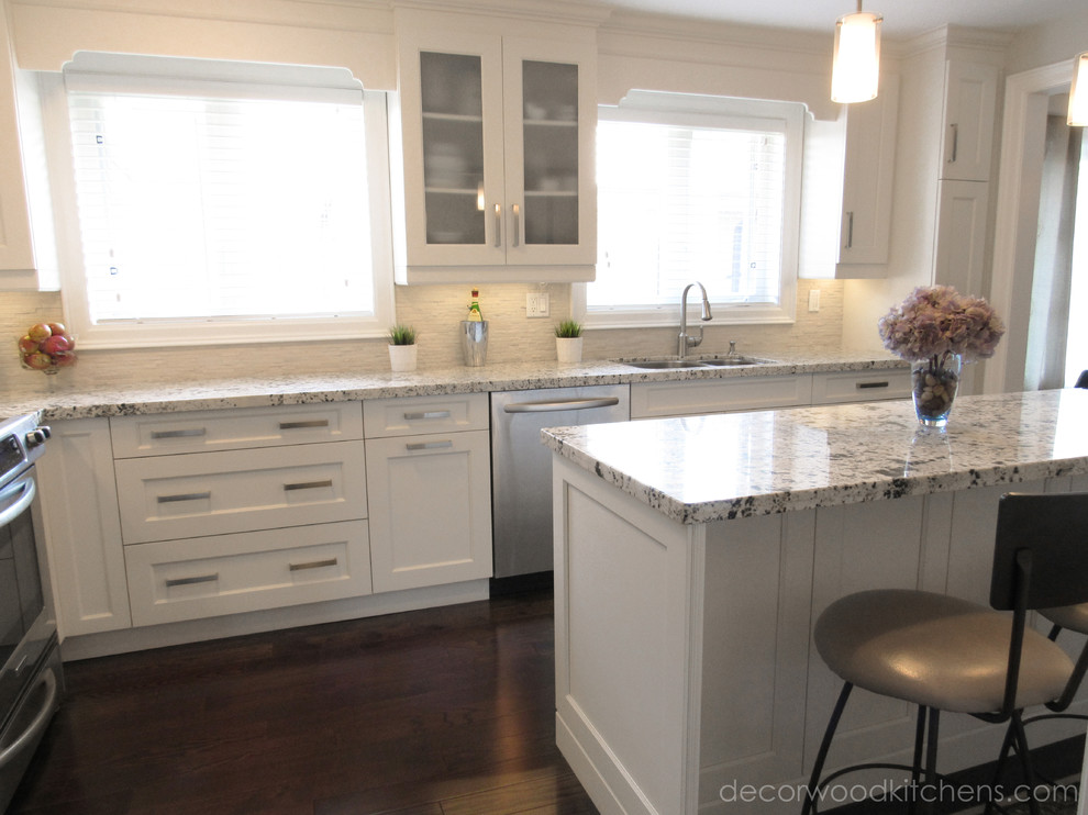 Inspiration for a mid-sized transitional l-shaped dark wood floor enclosed kitchen remodel in Toronto with an undermount sink, flat-panel cabinets, white cabinets, granite countertops, white backsplash, stone tile backsplash, stainless steel appliances and an island