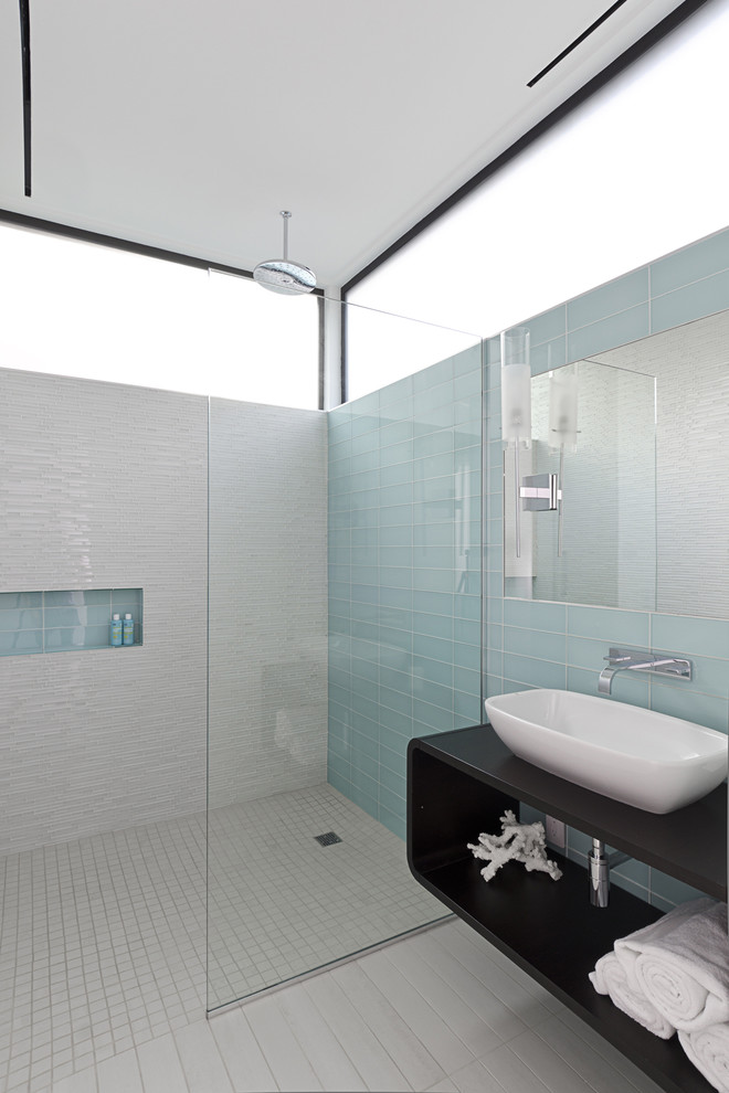 Modern bathroom in Houston with glass tile, wood benchtops, a curbless shower, blue tile, porcelain floors, white walls, grey floor and black benchtops.
