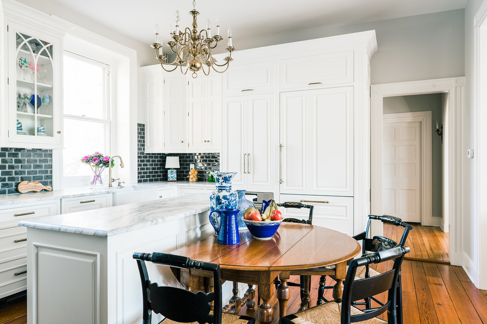 This is an example of a mid-sized transitional l-shaped eat-in kitchen in Philadelphia with a farmhouse sink, raised-panel cabinets, white cabinets, marble benchtops, grey splashback, ceramic splashback, stainless steel appliances, medium hardwood floors and with island.