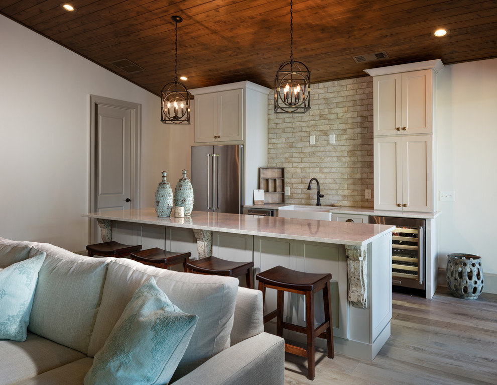 Photo of a small traditional single-wall open plan kitchen in Atlanta with light hardwood floors, brown floor, shaker cabinets, white cabinets, with island, a farmhouse sink, beige splashback, stainless steel appliances, white benchtop, quartz benchtops, porcelain splashback and vaulted.