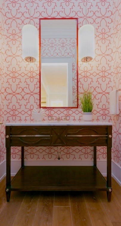 This is an example of a mid-sized transitional powder room in Charleston with furniture-like cabinets, brown cabinets, orange walls, medium hardwood floors, a drop-in sink, marble benchtops and brown floor.