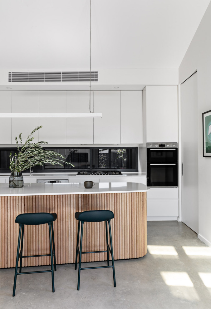 Inspiration for a medium sized modern galley kitchen/diner in Sydney with a submerged sink, flat-panel cabinets, white cabinets, quartz worktops, window splashback, stainless steel appliances, concrete flooring, an island, grey floors and white worktops.