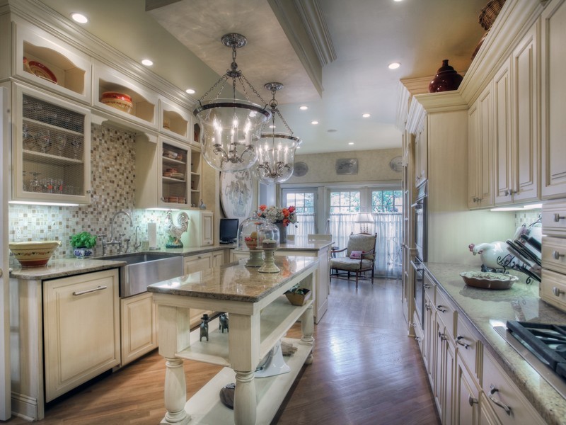 Design ideas for a mid-sized mediterranean u-shaped eat-in kitchen in Las Vegas with a farmhouse sink, raised-panel cabinets, medium wood cabinets, granite benchtops, beige splashback, stone tile splashback, panelled appliances, medium hardwood floors and with island.
