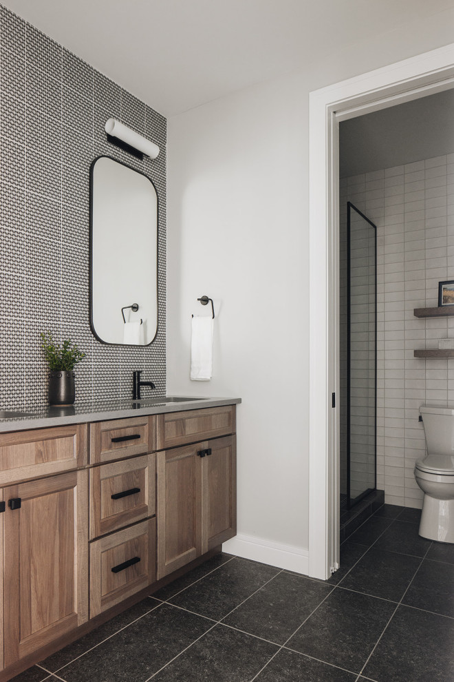 Bathroom - Modern bathroom featuring mosaic tile backsplash, wood vanity, two sinks, black faucets, gray countertops, black hardware, dark gray tile flooring, and stacked subway tile.