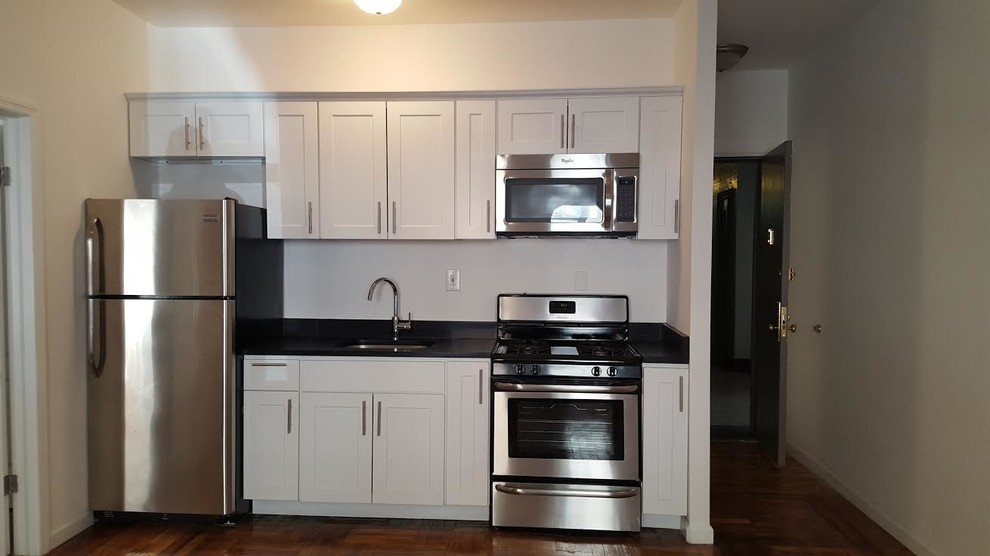 Example of a small transitional single-wall medium tone wood floor and brown floor enclosed kitchen design in New York with an undermount sink, shaker cabinets, white cabinets, solid surface countertops, stainless steel appliances, no island and black countertops