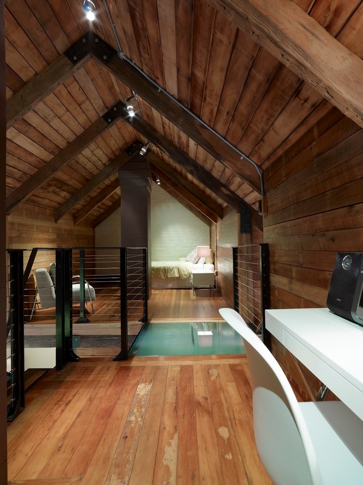 This is an example of a mid-sized eclectic loft-style bedroom in Sydney with brown walls, medium hardwood floors and brown floor.
