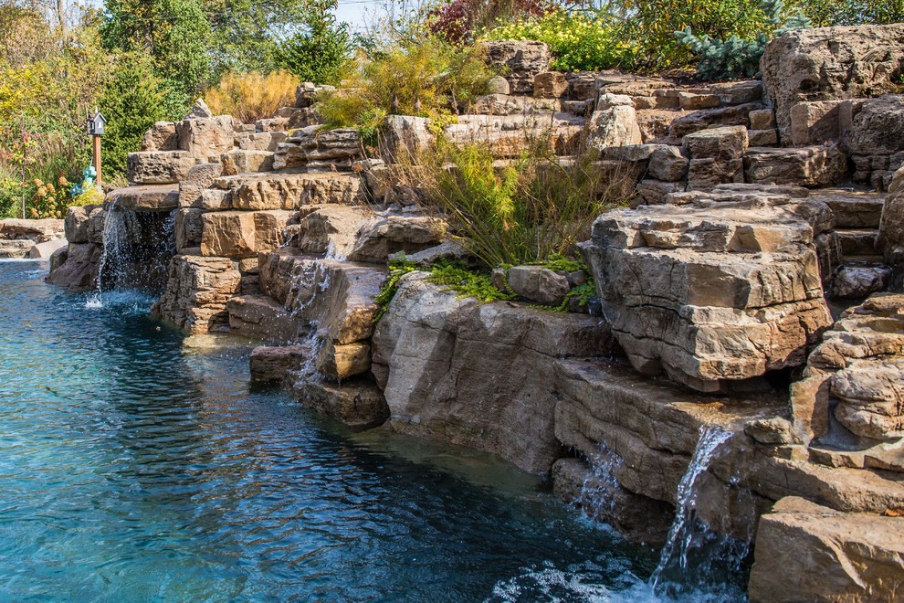 Design ideas for a large country backyard custom-shaped pool in St Louis with a water feature and natural stone pavers.
