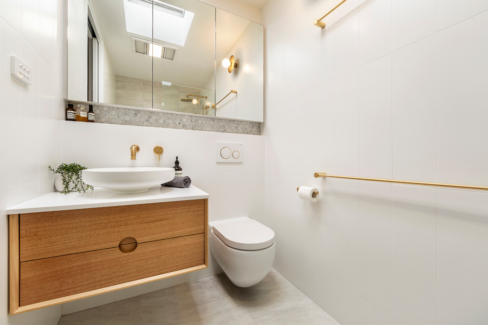 Inspiration for a contemporary 3/4 bathroom in Melbourne with flat-panel cabinets, medium wood cabinets, an alcove shower, a wall-mount toilet, gray tile, white tile, a vessel sink, beige floor and white benchtops.