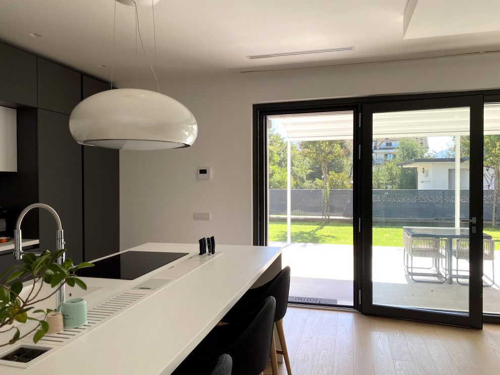 Design ideas for a large contemporary galley eat-in kitchen in Rome with an integrated sink, flat-panel cabinets, black cabinets, solid surface benchtops, white splashback, black appliances, light hardwood floors, with island and white benchtop.